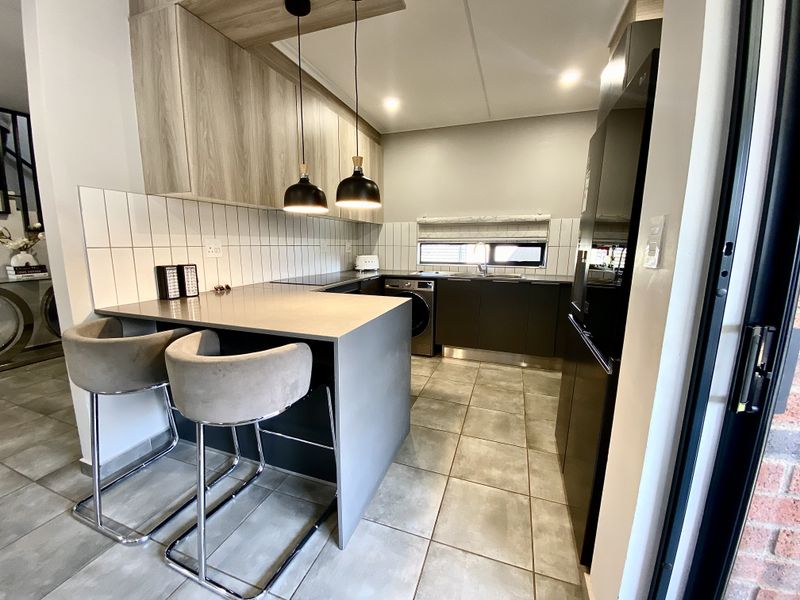 Modern kitchen featuring sleek cabinetry, stone countertops, a breakfast bar, tiled backsplash, and integrated appliances in a contemporary open-plan layout.