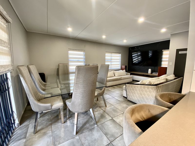 Spacious open-plan living and dining area featuring tiled flooring, recessed ceiling lighting, and a modern built-in media wall.