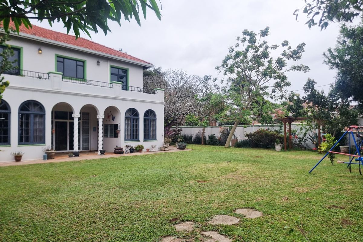 Spacious rear garden featuring a well-maintained lawn, paved patio area, and a two-story house with an arched colonnade and balcony.