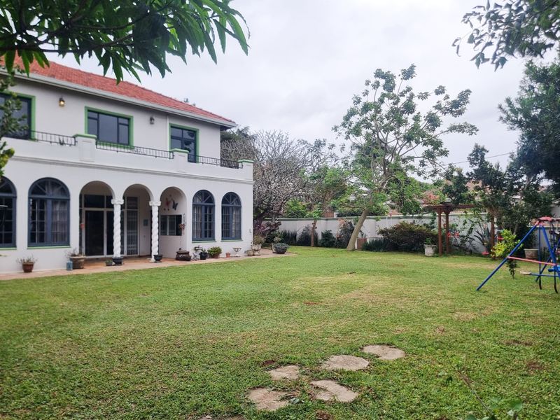 Spacious rear garden featuring a well-maintained lawn, paved patio area, and a two-story house with an arched colonnade and balcony.
