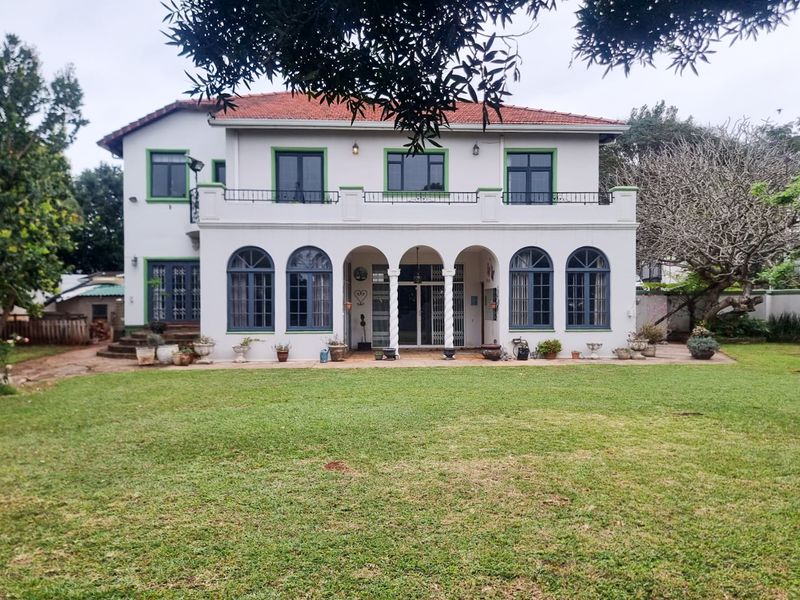 Rear view of a two-story house featuring a covered patio, arched windows, a balcony with metal railings, and a spacious lawn.