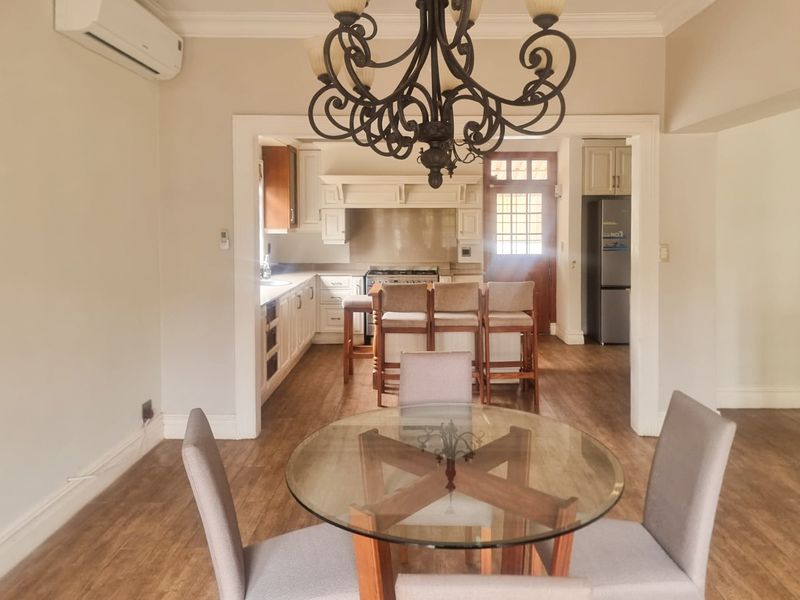 Open-plan living and kitchen area featuring timber-look flooring, a classic chandelier, split-system air conditioning, and a functional kitchen with built-in cabinetry.