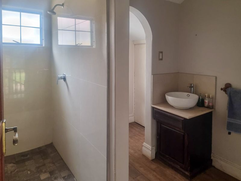 A functional bathroom featuring a walk-in shower with glass screen, tiled walls, and a vanity unit with a modern vessel sink.