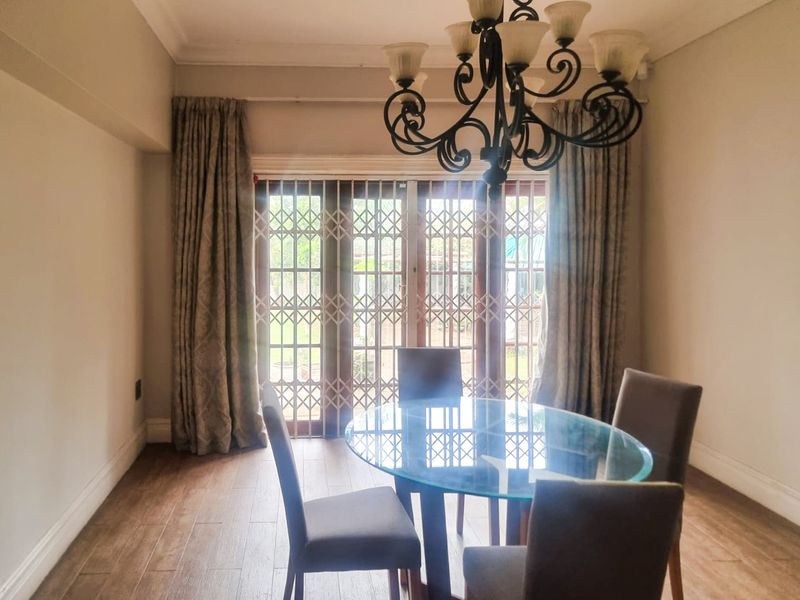 A well-lit dining room featuring laminate flooring, crown molding, and a decorative wrought iron chandelier, with access to the garden through a sliding glass door.