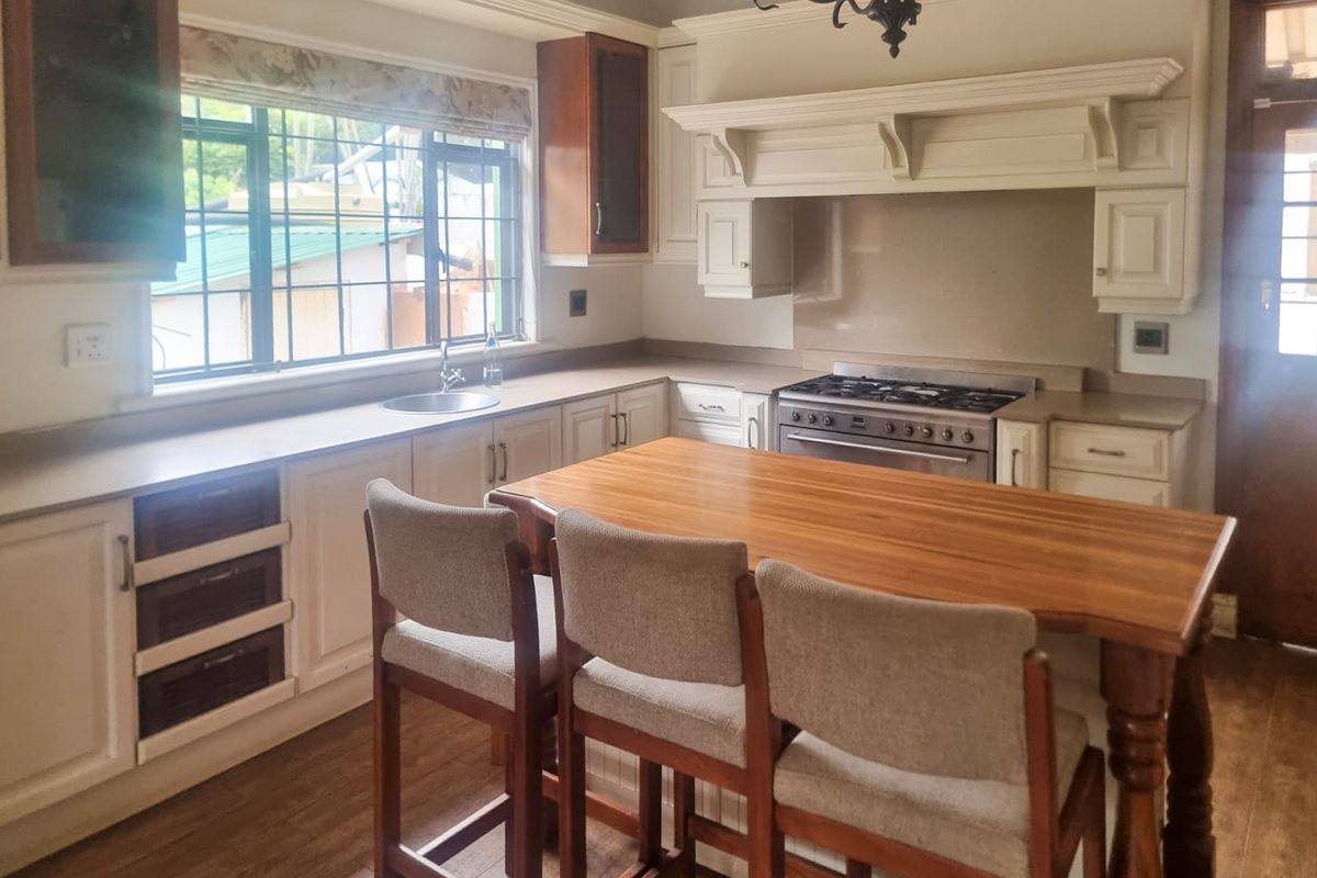 A traditional kitchen featuring cream cabinetry, a wooden island, gas stove with extractor hood, and large windows providing natural light.