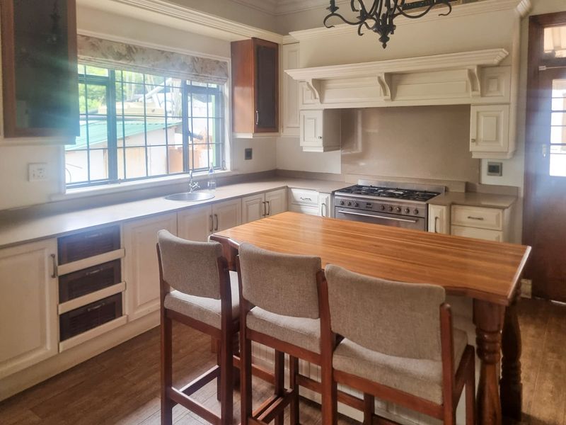 A traditional kitchen featuring cream cabinetry, a wooden island, gas stove with extractor hood, and large windows providing natural light.