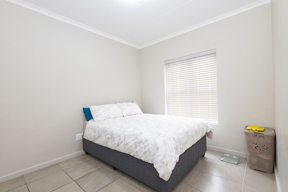 A clean and simple bedroom featuring neutral wall tones, tiled flooring, and a window fitted with venetian blinds.