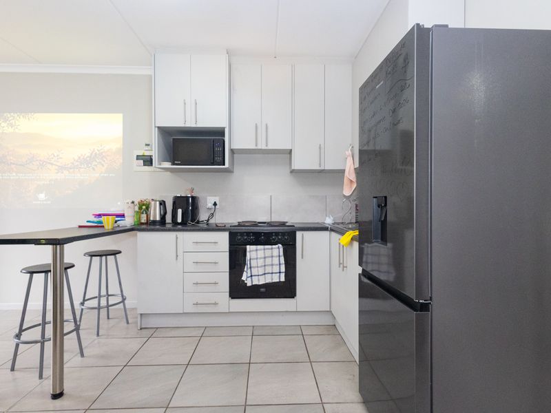 A functional kitchen featuring white cabinetry, dark countertops, a breakfast bar, and integrated appliances with tiled flooring.