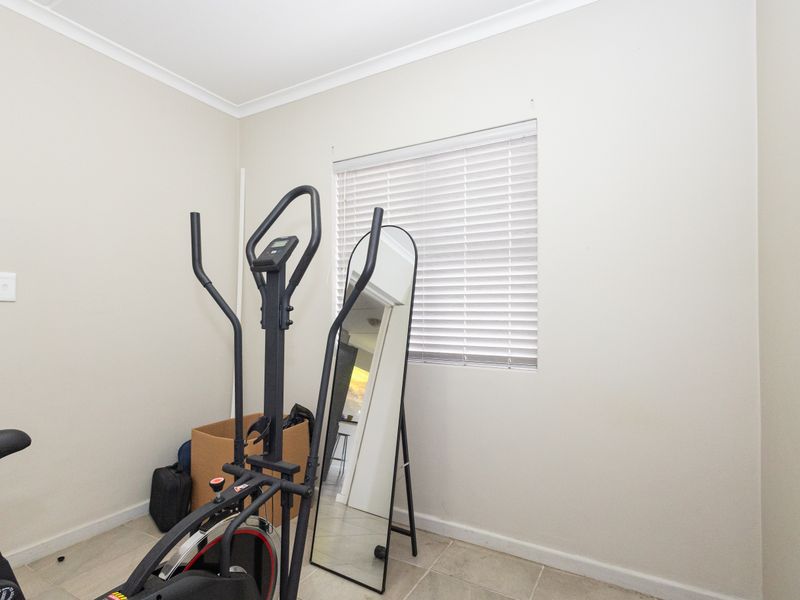 A neutral bedroom space featuring tiled flooring, cove cornicing, and venetian blinds, offering a versatile area for a home office or guest room.