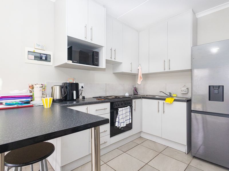 A functional kitchen featuring white cabinetry, dark laminate countertops, an integrated oven and hob, and tiled flooring.