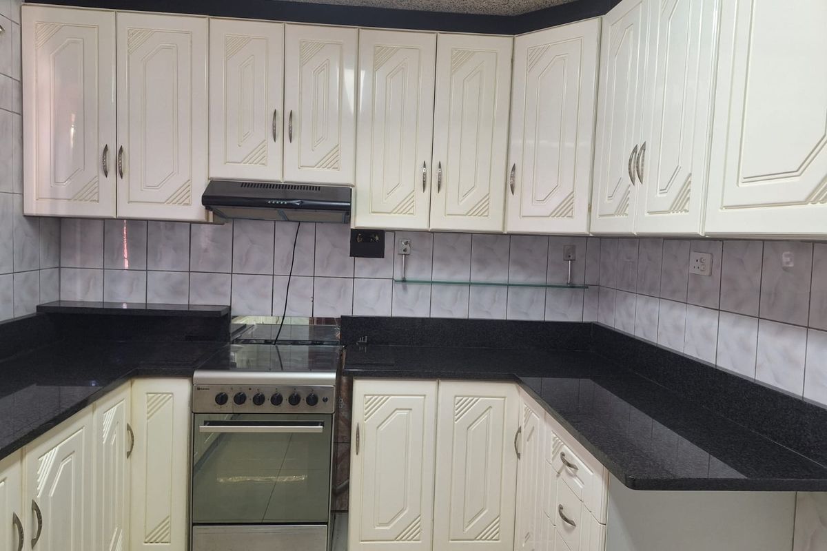 A functional kitchen featuring white cabinetry, dark granite countertops, a tiled backsplash, and a built-in extractor fan with a freestanding stove.