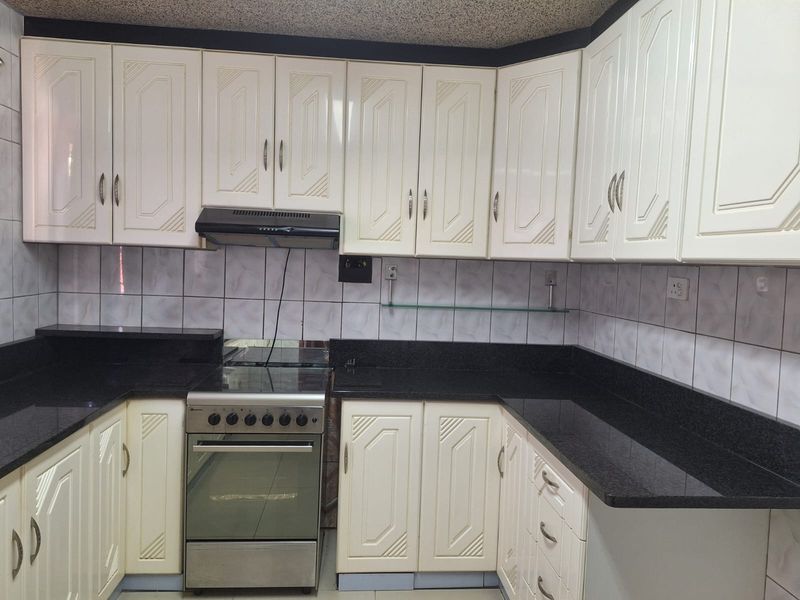 A functional kitchen featuring white cabinetry, dark granite countertops, a tiled backsplash, and a built-in extractor fan with a freestanding stove.