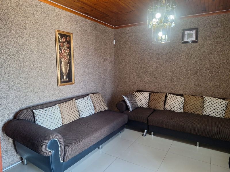 A living room featuring a timber tongue and groove ceiling, textured wall finishes, and tiled flooring, illuminated by a decorative chandelier.
