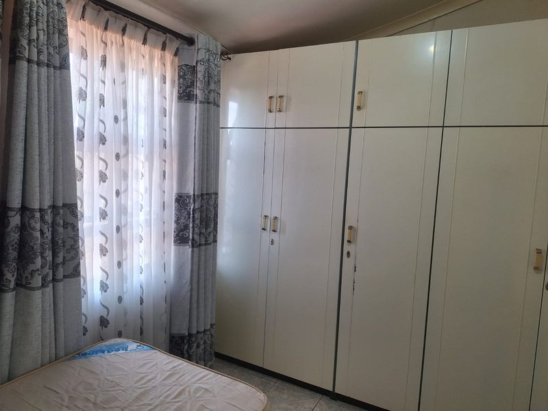 A bedroom featuring built-in cupboards with a white finish and tiled flooring, providing functional storage space.