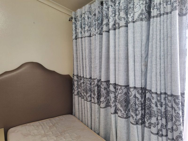 A bedroom interior featuring a headboard and floor-to-ceiling curtains.