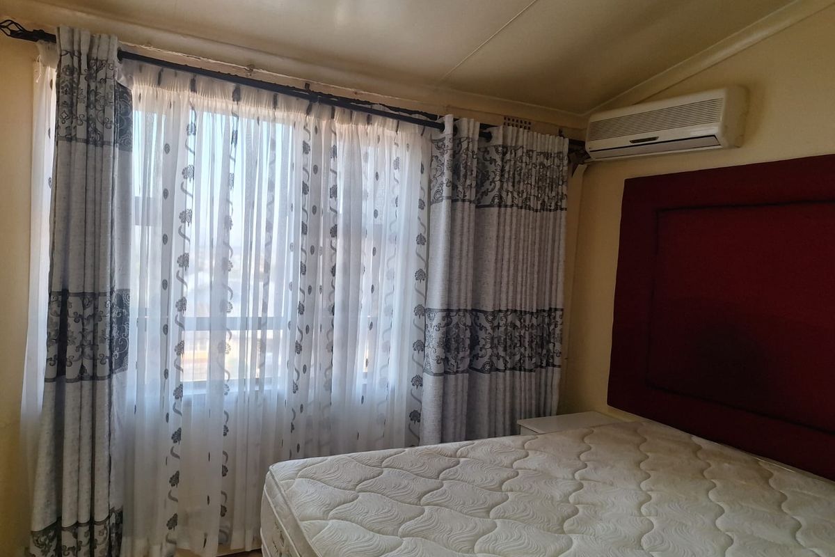 A bedroom featuring a wall-mounted split-system air conditioner and large window with curtain treatments.