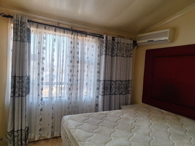 A bedroom featuring a wall-mounted split-system air conditioner and large window with curtain treatments.