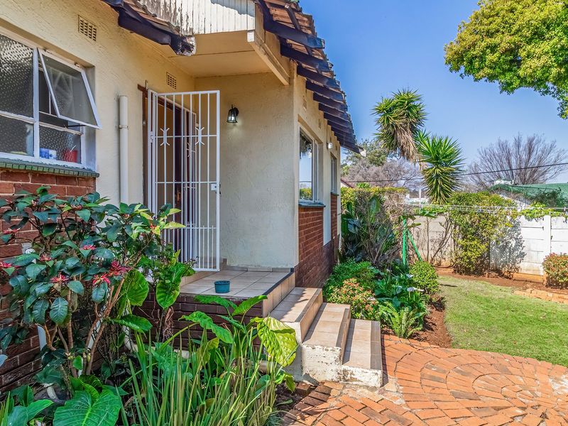 Rear exterior view of the house featuring a brick facade, tiled entrance steps with a security gate, and a landscaped garden with brick paving.