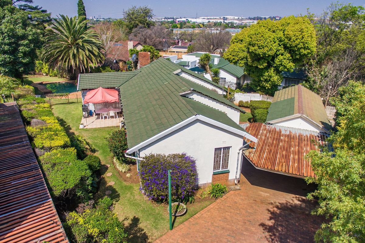 Aerial view of a residential property featuring a tiled roof house, brick driveway, carport, swimming pool, and established garden.