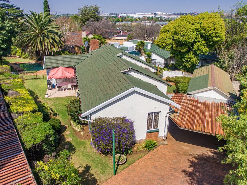 Aerial view of a residential property featuring a tiled roof house, brick driveway, carport, swimming pool, and established garden.