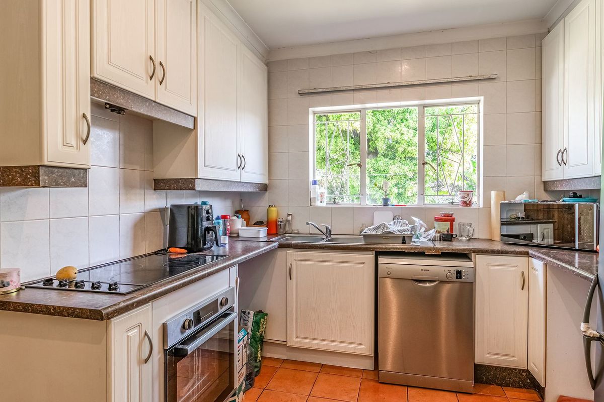 Functional kitchen featuring built-in cabinetry, electric hob, oven, and tiled finishes, offering a practical layout with natural light from the window.