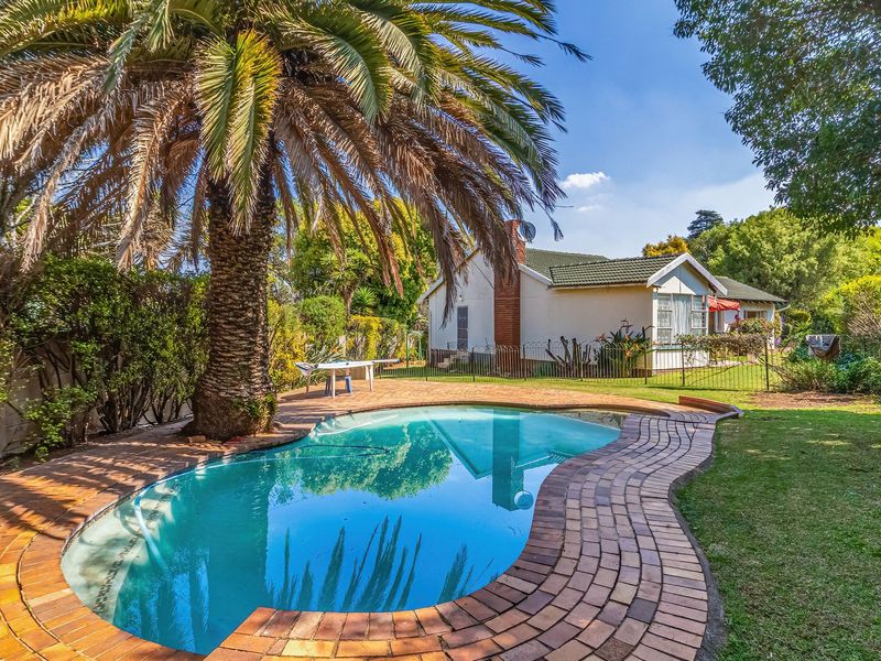 A well-maintained backyard featuring a swimming pool with brick paving, mature palm tree, and a clear view of the rear house elevation.