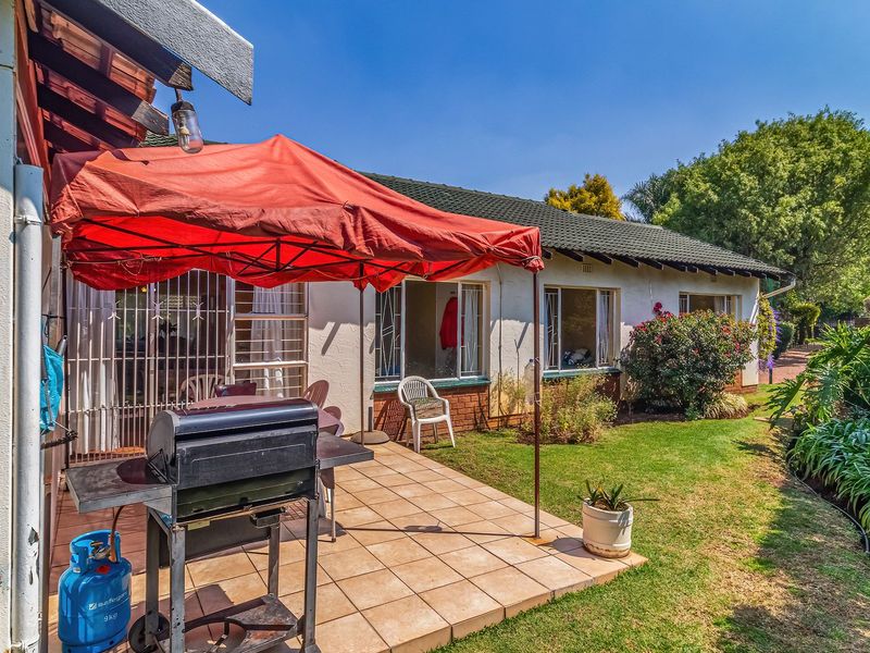 Rear view of the property featuring a tiled patio area, established garden, and direct access to the home through security-gated doors.