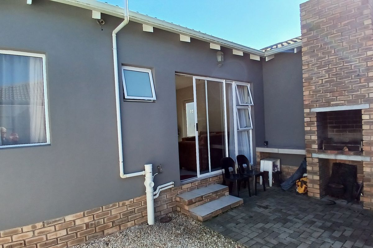 Rear exterior view of the townhouse featuring a paved patio area with a built-in brick fireplace and sliding door access to the living space.