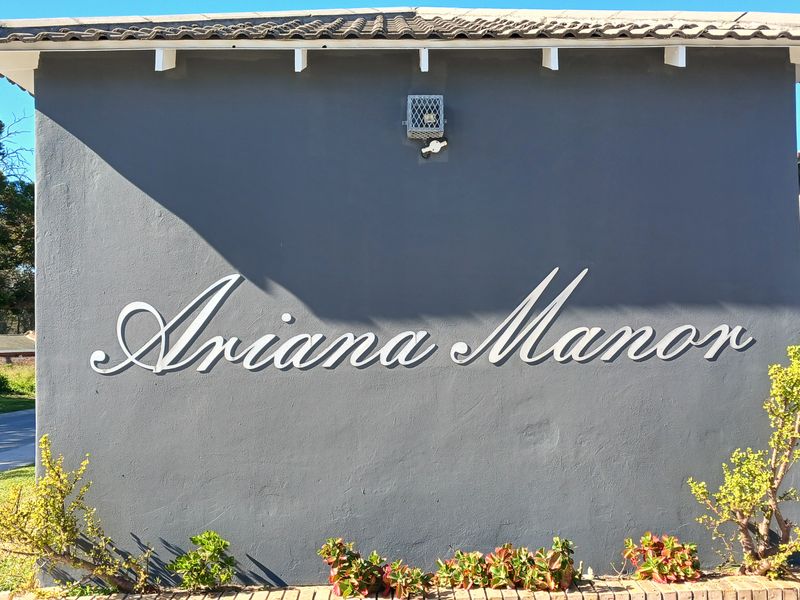 The front facade of Ariana Manor featuring a dark grey rendered wall with prominent building signage and a tiled roof overhang.