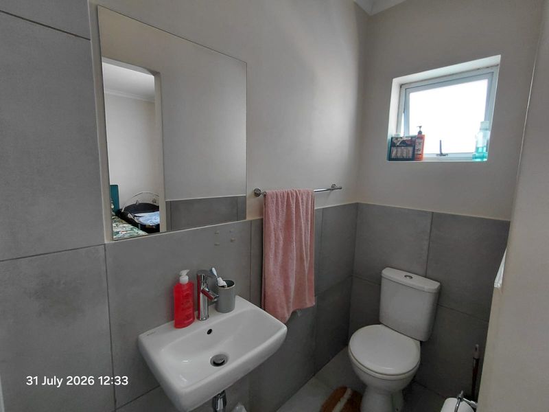A compact, modern bathroom featuring grey wall tiles, a wall-mounted basin, a toilet, and a functional window for natural light.