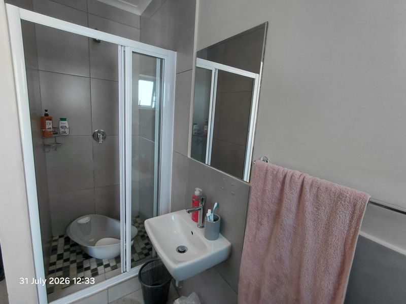A compact modern bathroom featuring a glass-enclosed shower, wall-mounted basin with mixer tap, and neutral grey wall tiling.
