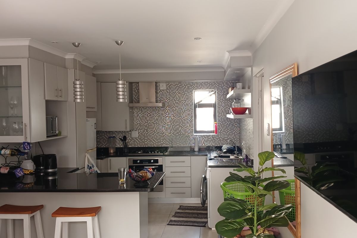 Modern kitchen featuring granite countertops, mosaic tile backsplash, built-in oven with gas hob, and a functional breakfast bar area.