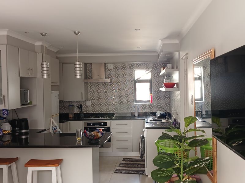 Modern kitchen featuring granite countertops, mosaic tile backsplash, built-in oven with gas hob, and a functional breakfast bar area.