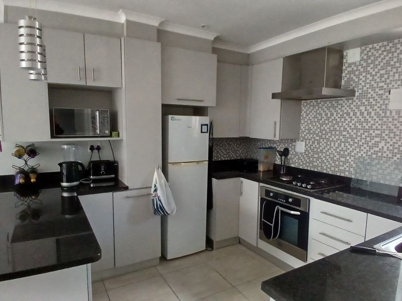 A functional kitchen featuring modern grey cabinetry, black granite countertops, a mosaic tile backsplash, and integrated stainless steel appliances.