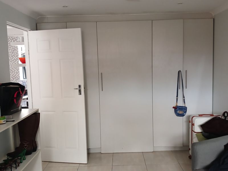 A bedroom featuring neutral tiled flooring, recessed ceiling lighting, and extensive floor-to-ceiling built-in cupboards providing ample storage space.