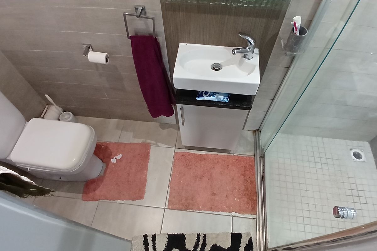 Compact bathroom featuring a modern vanity basin, toilet, and a glass-enclosed shower with neutral wall and floor tiling.