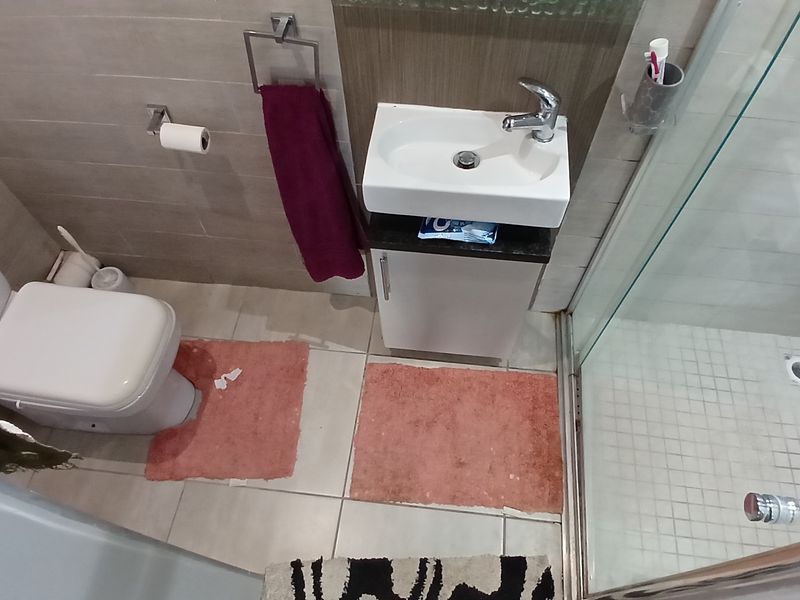 Compact bathroom featuring a modern vanity basin, toilet, and a glass-enclosed shower with neutral wall and floor tiling.