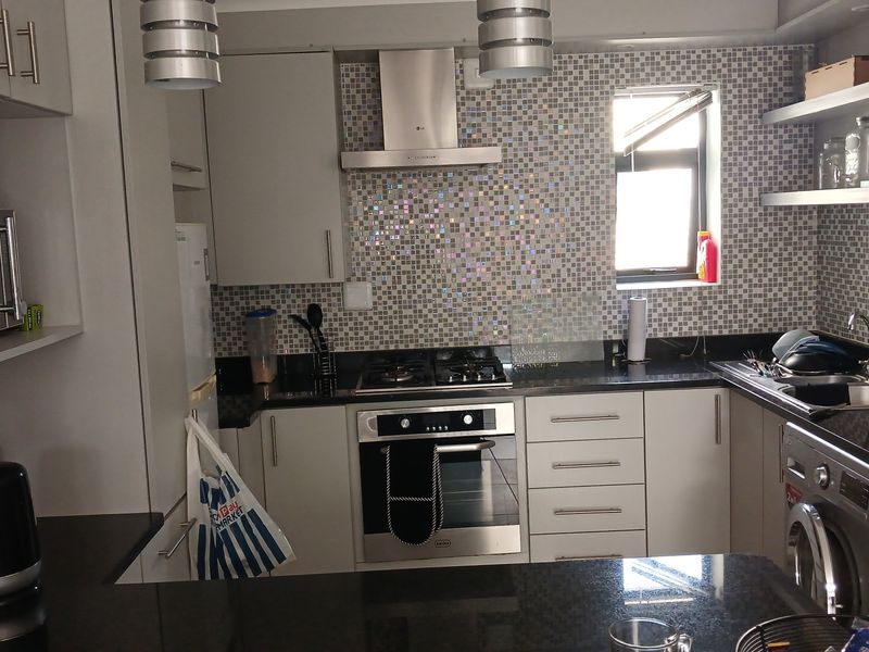 Modern kitchen featuring granite countertops, mosaic tile backsplash, built-in oven with gas hob, stainless steel extractor fan, and integrated laundry appliance.