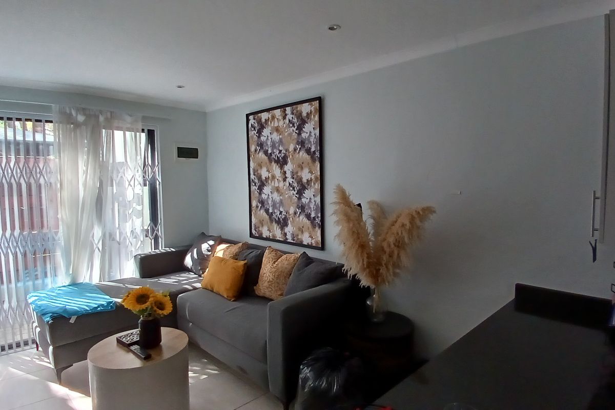 Open plan living area featuring tiled flooring, recessed downlights, and a sliding glass door with a security gate leading to the exterior.