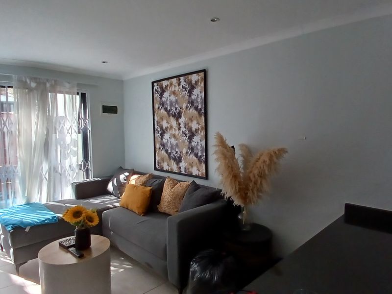 Open plan living area featuring tiled flooring, recessed downlights, and a sliding glass door with a security gate leading to the exterior.