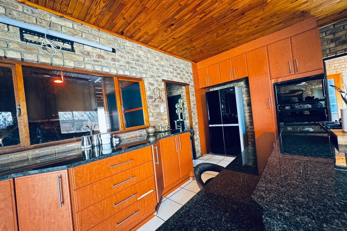 A kitchen featuring timber cabinetry, granite countertops, exposed brick walls, and a timber ceiling, offering a rustic aesthetic with built-in oven and ample storage.
