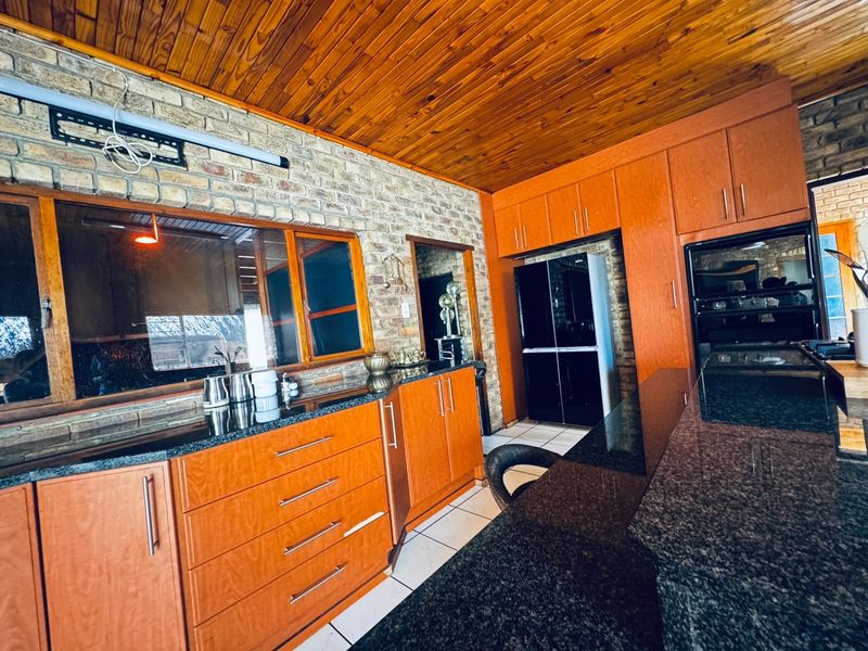 A kitchen featuring timber cabinetry, granite countertops, exposed brick walls, and a timber ceiling, offering a rustic aesthetic with built-in oven and ample storage.