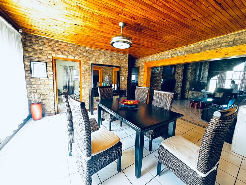 Dining area featuring exposed brick walls, a warm timber ceiling, and ceramic tiled flooring, connecting to an adjacent living space.