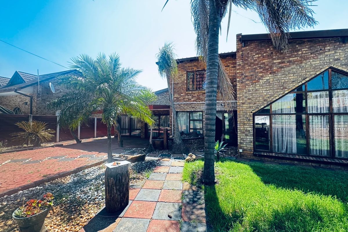 Rear view of a face brick house featuring a paved garden path, large feature windows, and established landscaping.