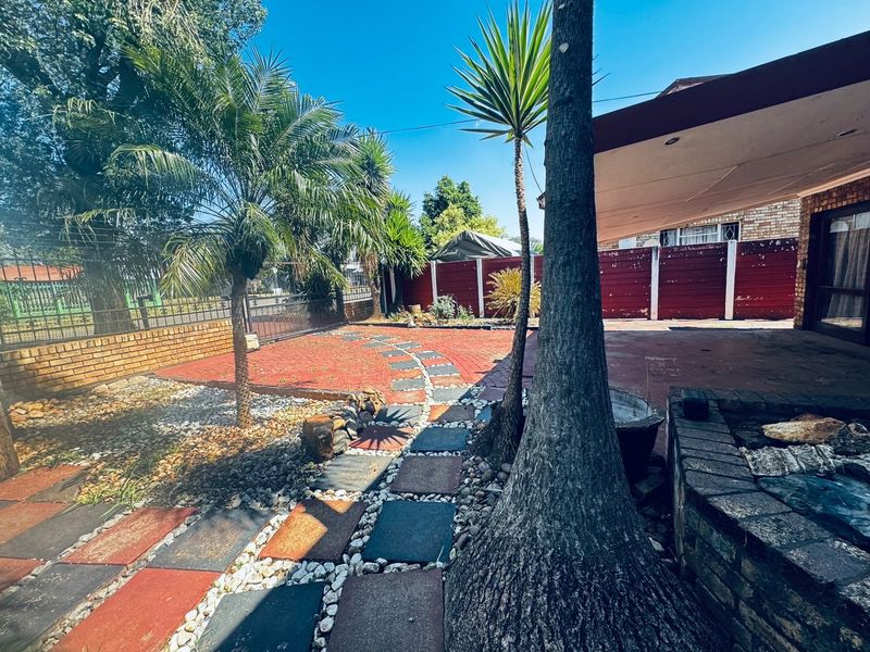 Rear garden area featuring a paved patio, covered outdoor space, and established landscaping with brick boundary walls.