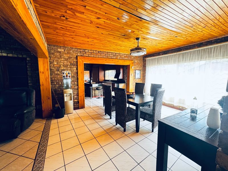 Open plan living and dining area featuring exposed brick walls, timber ceiling, and large sliding doors providing natural light.