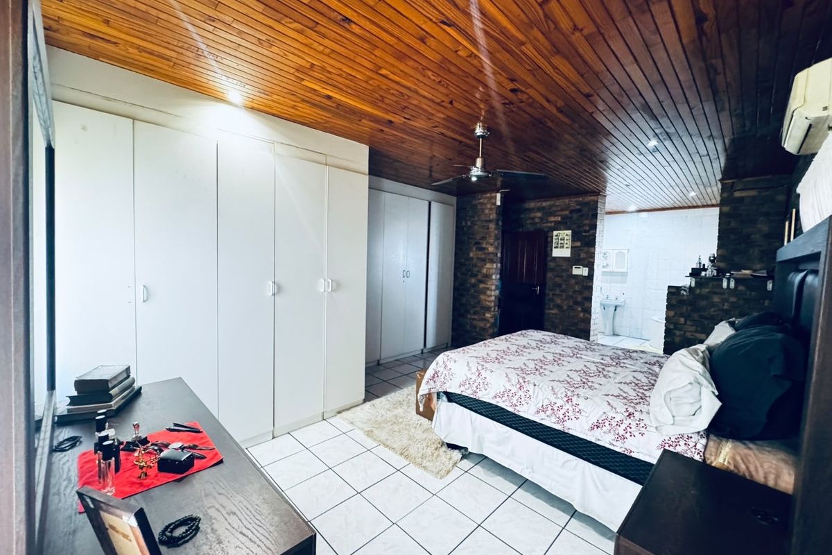 Spacious bedroom featuring a timber ceiling, built-in cupboards, tiled flooring, and an exposed brick wall leading to an en-suite bathroom.