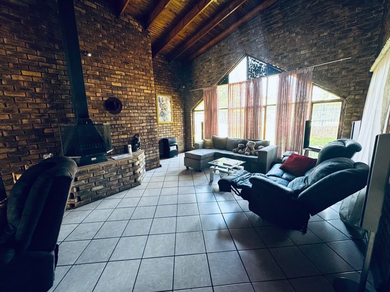 Spacious living room featuring exposed brick walls, a vaulted timber ceiling, tiled flooring, and a prominent freestanding fireplace with large windows.