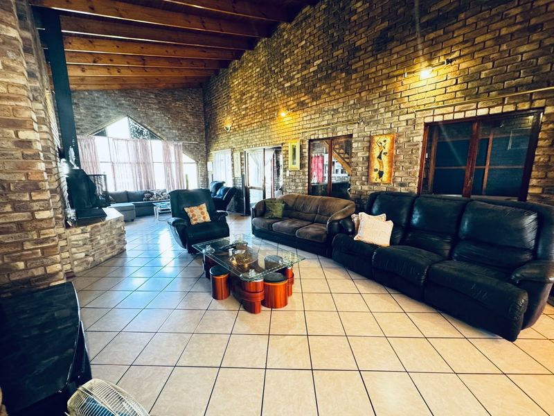 Spacious living room featuring high exposed timber beam ceilings, rustic face brick walls, ceramic tiled flooring, and a prominent freestanding fireplace.