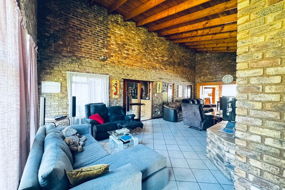 Spacious living area featuring high exposed timber beam ceilings, rustic exposed brick walls, tiled flooring, and a stone-clad fireplace base.